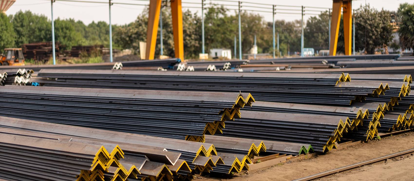 Steel angles stacked in a yard under a gantry crane